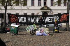 Art Bühne mit Banner "wir machen weiter>" Mikrofon, Foto von Karsten, cola Flasche, kleines Banner "Lieber in Bäumen wohnen statt Wälder roden", Bauwagen aus Pppkarton, Karstens fahrrad