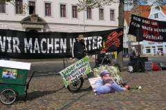 Art Bühne mit Banner "wir machen weiter>" Mikrofon, Foto von Karsten, cola Flasche, kleines Banner "Lieber in Bäumen wohnen statt Wälder roden", Bauwagen aus Pppkarton, Karstens fahrrad
