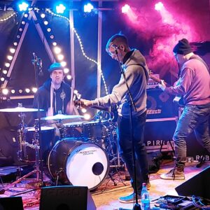 Bands auf der Bühne mit Schlagzeug, E-Guitarre, bunter Rauch, Licht in From von Anachie A im Hintergrund